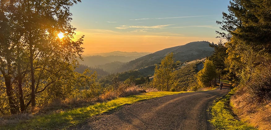 A paved trail with views of hillsides and orange skies.